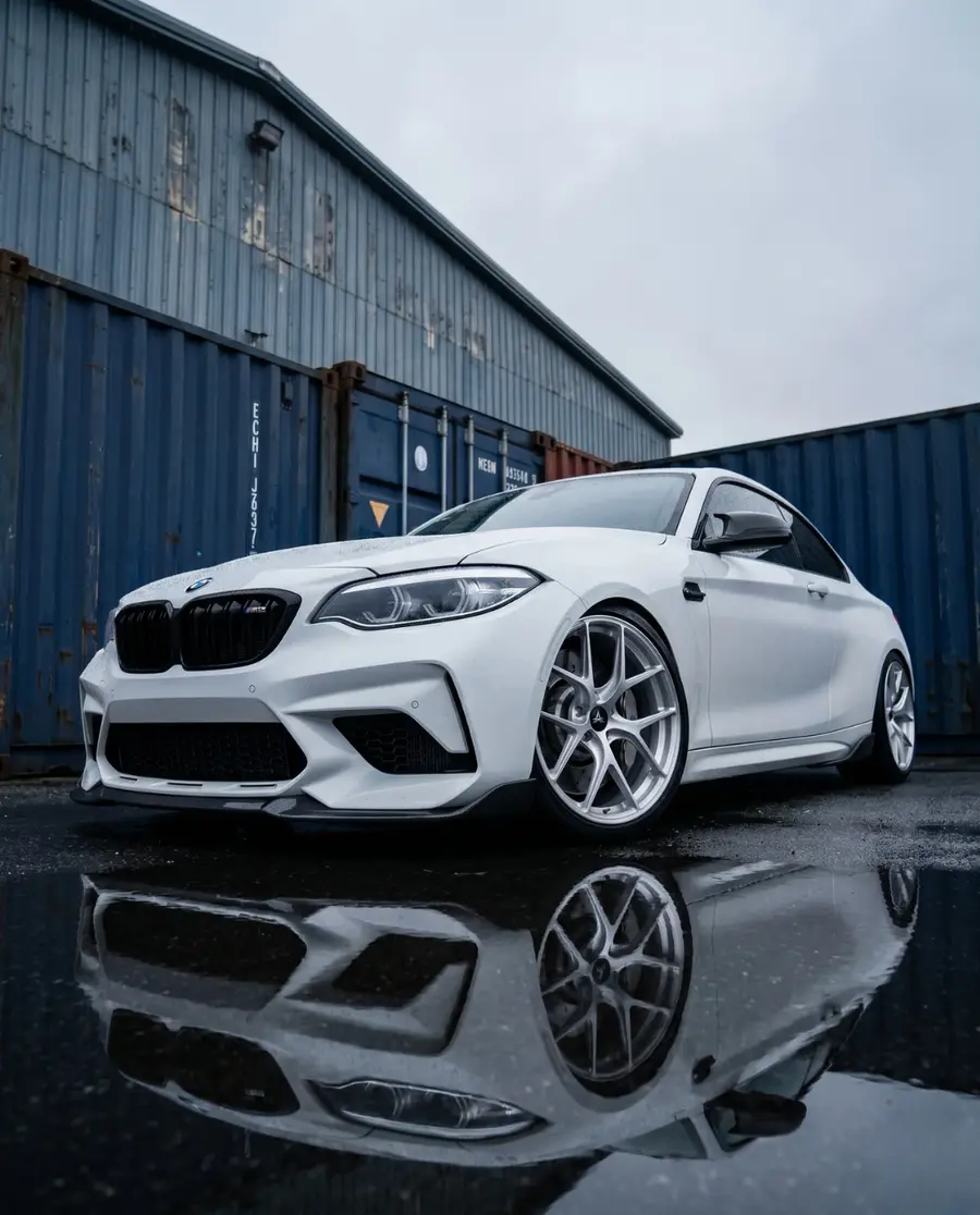 BMW M2 blanco con AXYS FAN Silver sobre piso mojado